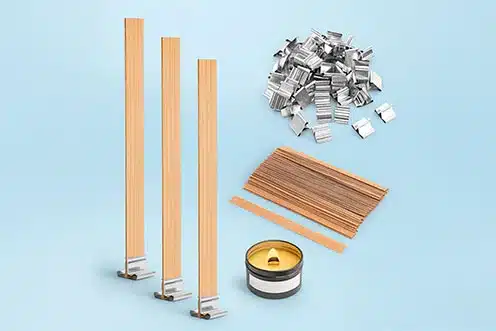 Mechas de madera con soportes metálicos y rollo de pabilo para velas artesanales sobre fondo azul